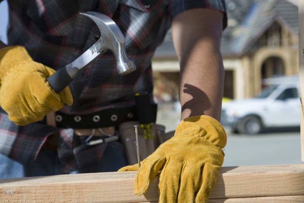 Construction worker hammering nail to wooden plank on construction site